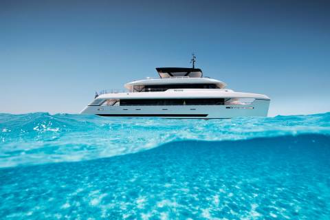 A sleek white yacht floats on a clear blue ocean, with the water's surface creating a dynamic foreground against a serene sky.
