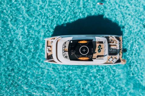 A luxurious catamaran floats on crystal-clear turquoise water, with a small paddleboard visible in the distance.