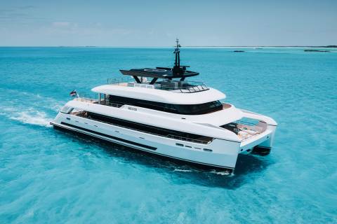 A sleek white catamaran yacht glides through crystal-clear turquoise waters under a bright blue sky.