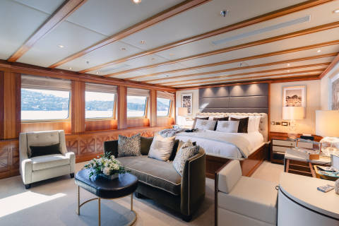 A luxurious bedroom with a plush sofa and armchair in the foreground, and a large bed with a scenic view of the water and hills in the background.