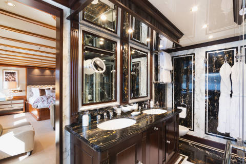 A luxurious bathroom with a marble vanity and dual sinks is visible in the foreground, while a bedroom with a large bed and seating area is seen through an open doorway in the background.