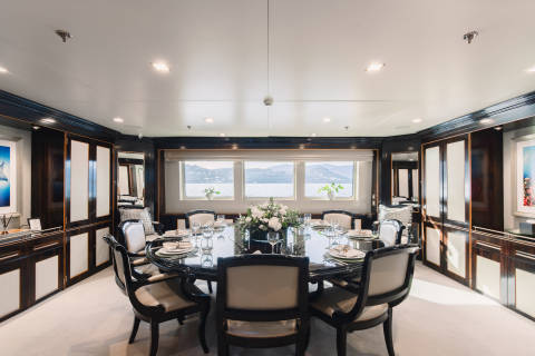 A formal dining table set for a meal is in the foreground, while a scenic view of islands and water is visible through the windows in the background.