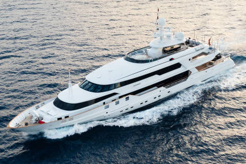 A large white yacht cruises through calm blue water, leaving a foamy wake behind it.