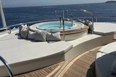 A circular jacuzzi with plush cushions sits on the deck of a yacht, with the calm blue ocean stretching to the horizon in the background.