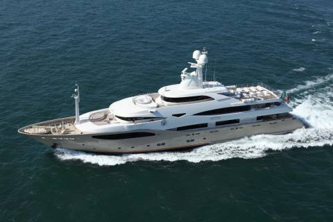 A large white yacht cruises through calm blue water, leaving a foamy wake behind it.