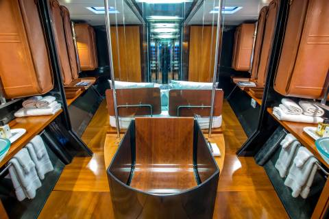 A luxurious yacht cabin features a central wooden bathtub in the foreground and a mirrored hallway with plush seating in the background.