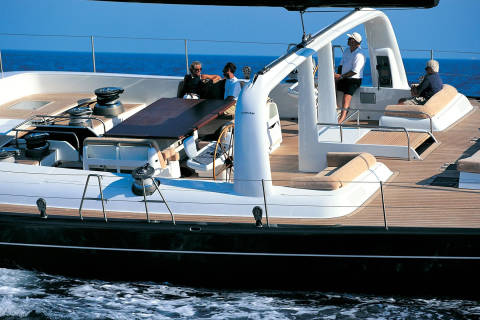 Four people relax on the deck of a large sailboat with the blue ocean stretching out behind them.