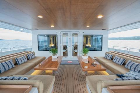 Luxurious outdoor seating with plush cushions and wooden tables fills the foreground, while the background reveals a serene ocean view with distant islands under a bright sky.