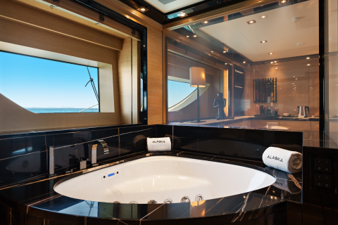 A luxurious bathtub with fluffy white towels sits in the foreground, while the background reveals a kitchenette and a window with a view of the ocean.
