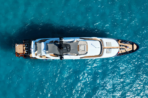 A luxurious white yacht with dark accents floats on the clear turquoise ocean.