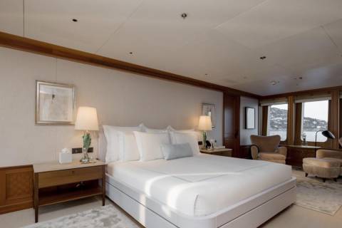 A luxurious bedroom with a large bed in the foreground and windows overlooking a coastal town in the background.