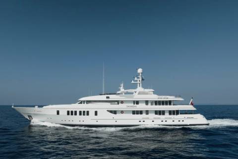 A large white yacht cruises through calm blue water with a clear blue sky in the background.