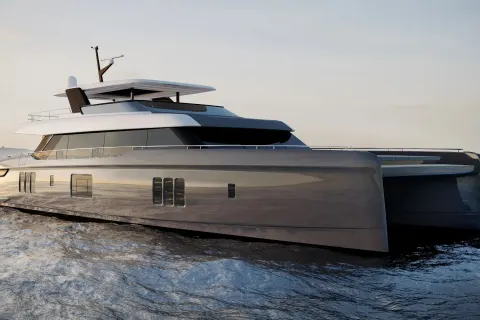 A sleek, modern catamaran yacht glides across calm, rippling water under a soft, overcast sky.