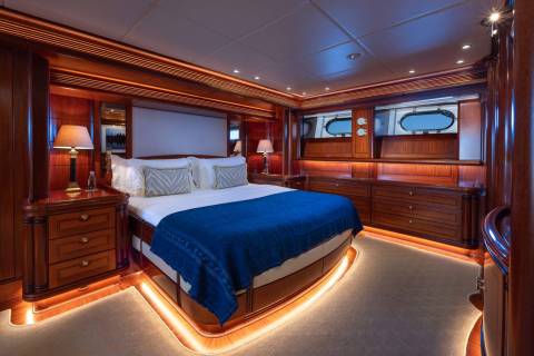 A luxurious yacht bedroom with a king-sized bed in the foreground and oval windows in the background.