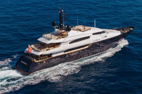 A luxury yacht named "Alaska" cruises through deep blue ocean waters, leaving a white wake in its path.