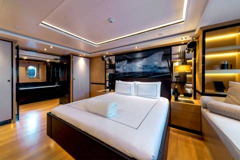 A modern bedroom features a neatly made white bed in the foreground, set against a background of sleek cabinetry, warm ambient lighting, and a large piece of art.