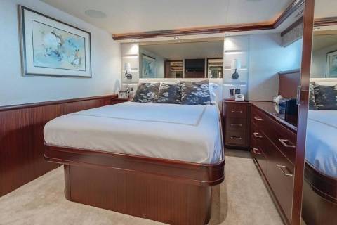 A neatly made bed with white linens and patterned pillows sits in the foreground of a luxurious bedroom featuring dark wood paneling and a large mirror in the background.