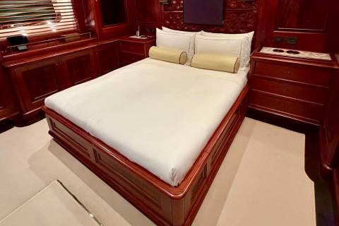 A bed with white linens and yellow bolster pillows sits in a room with polished mahogany wood paneling and cabinetry.