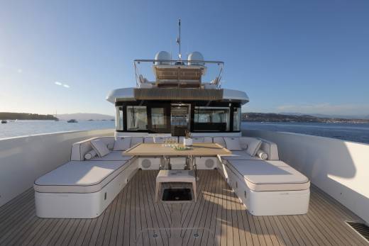A luxurious yacht deck offers a comfortable seating area with a table set for drinks and snacks, overlooking a serene bay.