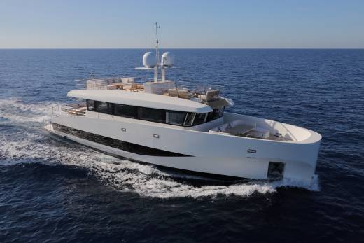 A sleek white superyacht glides through the deep blue ocean on a clear, sunny day.