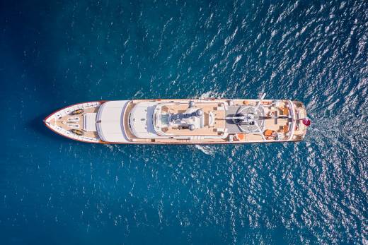 An opulent yacht glides through the deep blue ocean, its helipad and deck furniture hinting at luxurious adventures.