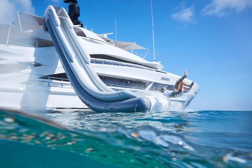 A person joyfully slides down an inflatable yacht slide into the clear blue ocean.
