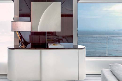 A stylish white credenza with a modern lamp and art piece sits beside a large window overlooking the serene ocean.
