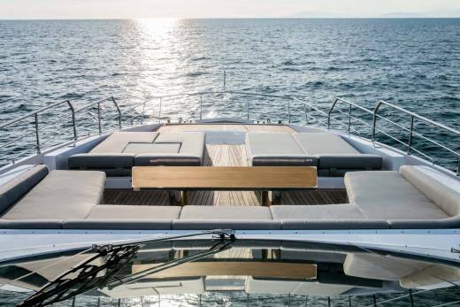 Relax on the spacious deck of this luxury yacht, with plush seating and a wooden table overlooking the shimmering ocean.