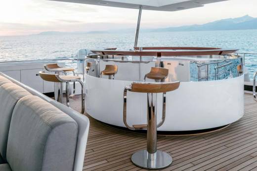 A luxurious yacht bar with sleek seating and polished chrome stools offers a perfect spot to enjoy the sunset over the ocean.