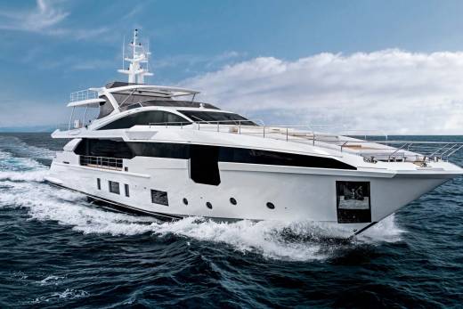 A sleek white yacht cuts through the deep blue ocean waves under a partly cloudy sky.