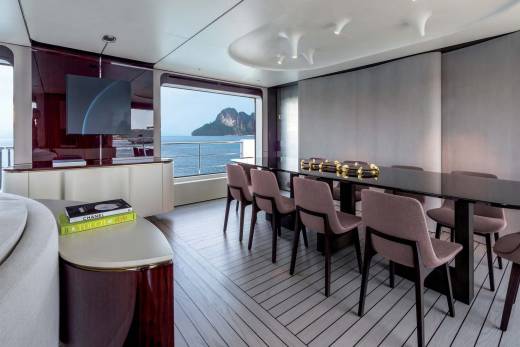 A modern dining area on a yacht offers a stunning view of a tropical island through a large panoramic window.