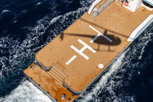 A helicopter's shadow falls across the helipad of a luxurious yacht cruising through the deep blue ocean.