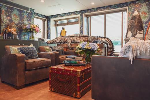 A luxurious living room features leather armchairs, a decorative alligator, and exotic floral arrangements against a jungle-themed wallpaper.