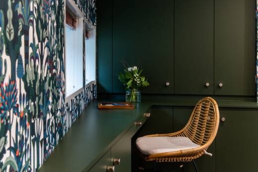 A stylish rattan chair sits beside a dark green desk adorned with a bouquet of white tulips and greenery.