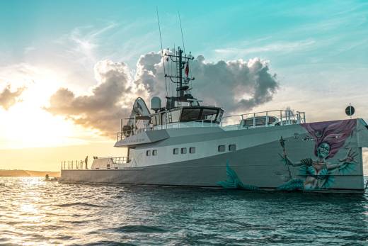 A striking mermaid mural adorns the stern of the Pink Shadow yacht as it sails through the tranquil ocean at sunset.