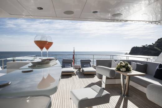 Two glasses of rosé sparkle on a yacht's deck, overlooking a sun-drenched sea and a rocky coastline.