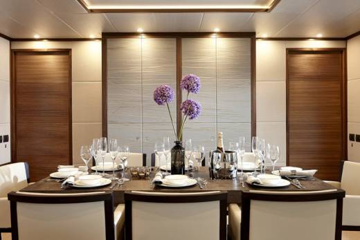 A beautifully set dining table awaits guests aboard a luxurious yacht, complete with fine china, crystal glasses, and a chilled bottle of champagne.