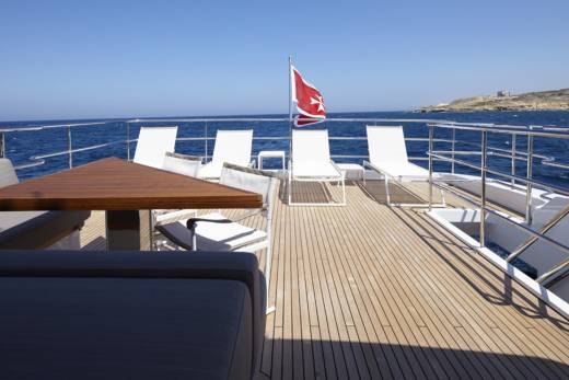 Relax on the spacious deck of this luxury yacht, complete with comfortable seating and a striking red flag against the azure sea.