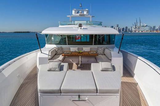 Relax on the spacious deck of this luxurious yacht, complete with plush seating and a dining area, overlooking a distant city skyline.