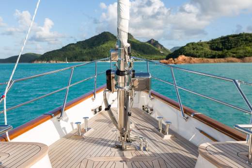 Sailing on turquoise waters, the bow of a luxurious yacht cuts through the waves towards lush green islands under a bright blue sky.