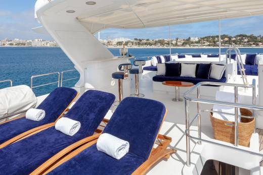 Relax on plush blue loungers with rolled towels, overlooking a picturesque coastal town from the deck of a luxurious yacht.
