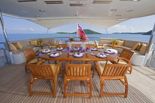 A beautifully set dining table awaits guests on the deck of a yacht, with a stunning ocean view.