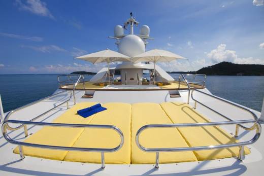 Luxurious yellow sunbeds await on the deck of a yacht, offering a perfect spot to relax under the bright blue sky.