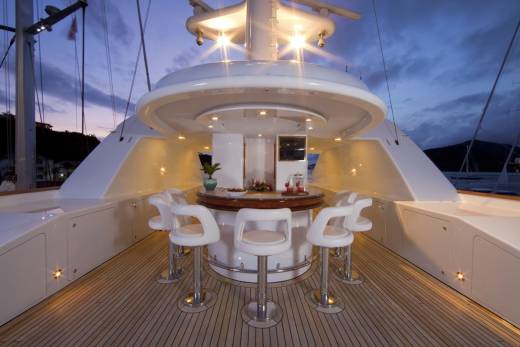Elegant white bar stools surround a polished wooden bar on a yacht deck as twilight descends.