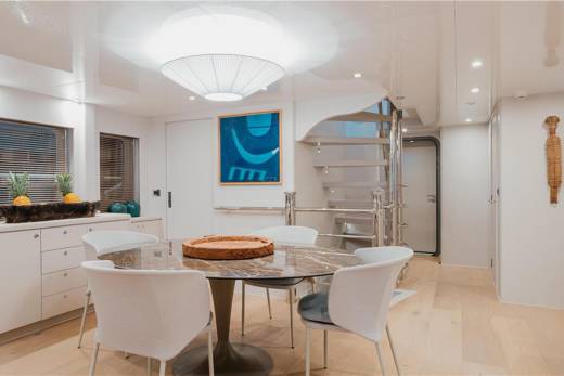 A modern dining area features a marble-topped table surrounded by sleek white chairs, with a spiral staircase in the background.