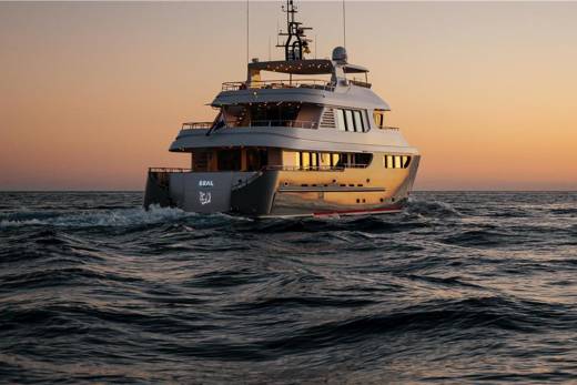 A sleek yacht glides through choppy waters at sunset, its windows reflecting the warm, golden light.