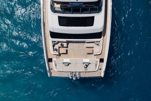 Two people relax on the spacious deck of a luxurious yacht cruising through clear blue waters.