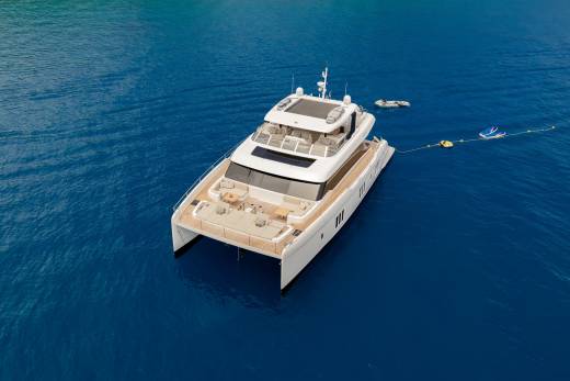 A luxurious white catamaran yacht floats serenely on the deep blue ocean, surrounded by inflatable water toys.