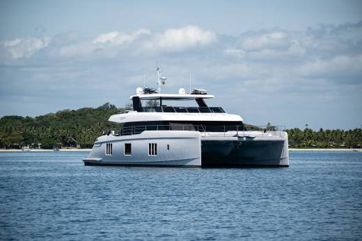 A sleek, modern catamaran glides through calm blue waters near a tropical island paradise.