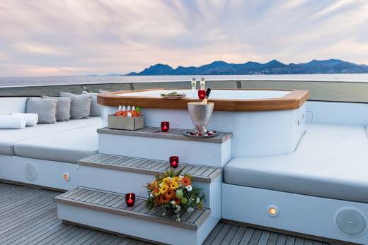 Champagne and a floral bouquet await on the deck of a luxury yacht as the sun sets over the distant coastline.